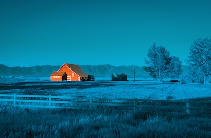 A barn sits in an agricultural field in front of mountains